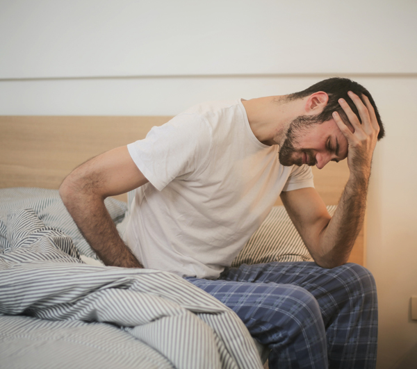 Man hunched over while sitting on bed due to pain and fatigue